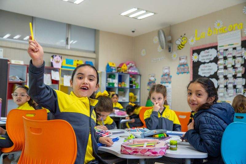 Estudiante en uniforme escolar amarillo y azul concentrada durante clase en el aula del colegio