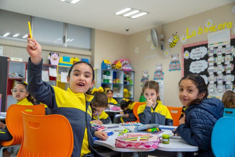 Estudiante en uniforme escolar amarillo y azul concentrada durante clase en el aula del colegio